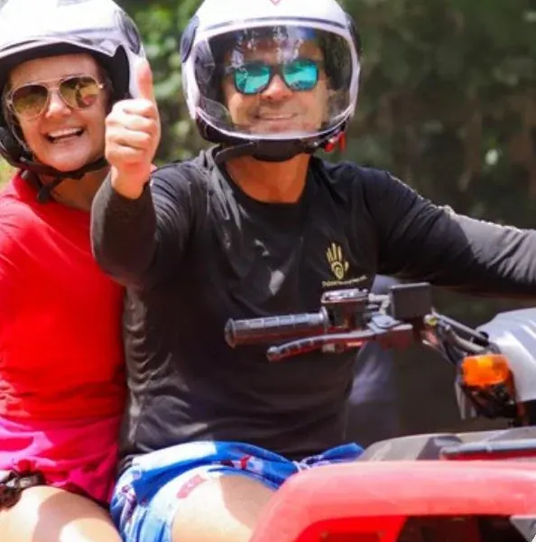 Helmeted couple giving thumbs up while seated on a double ATV