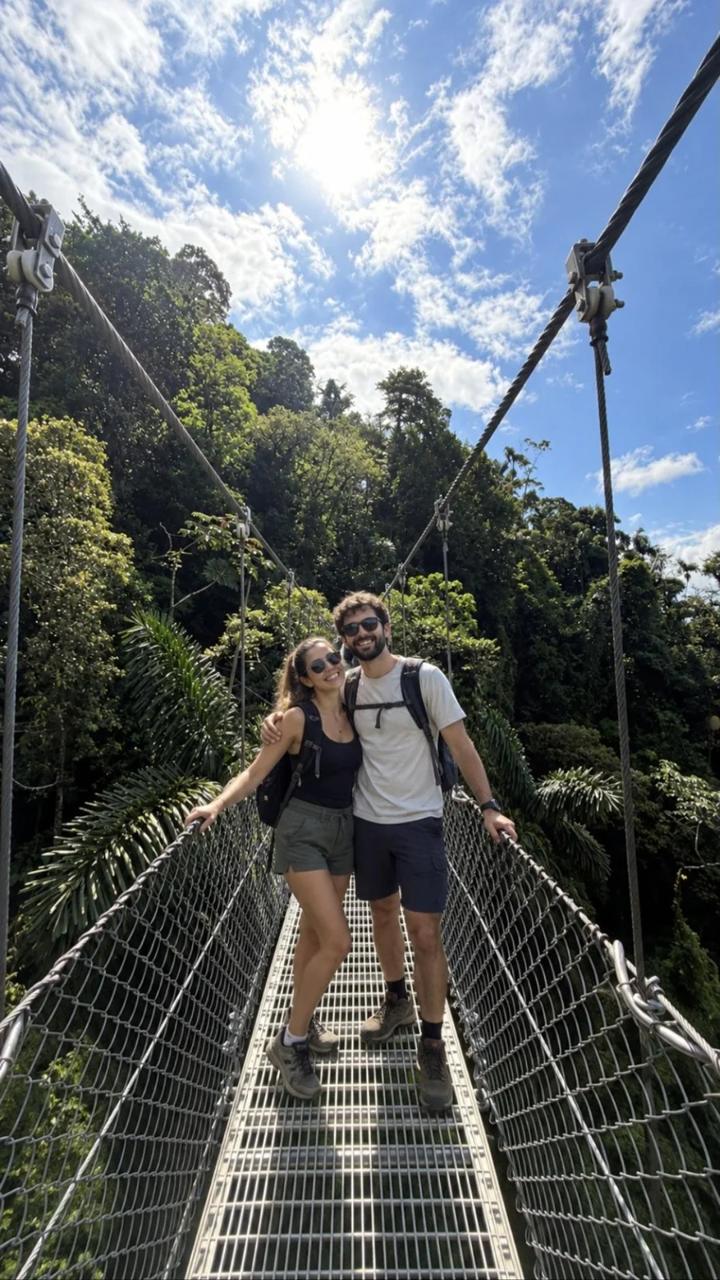 Couple smiling on a hanging bridge above the Arenal rainforest canopy