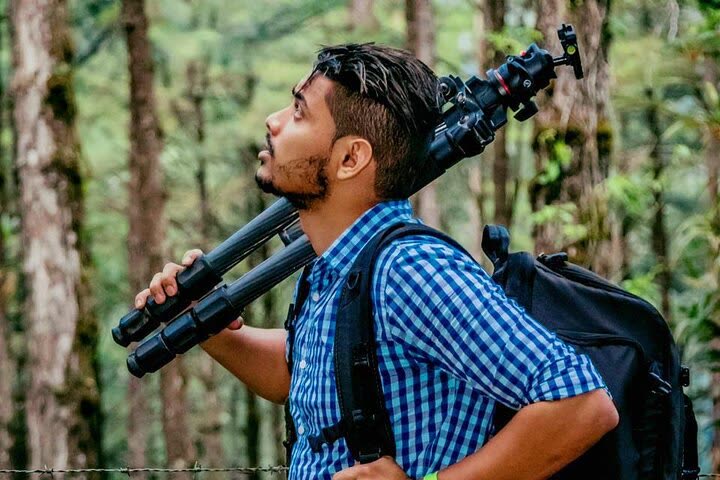 Elias Peña walking through the forest with his tripod over his shoulder during a field outing